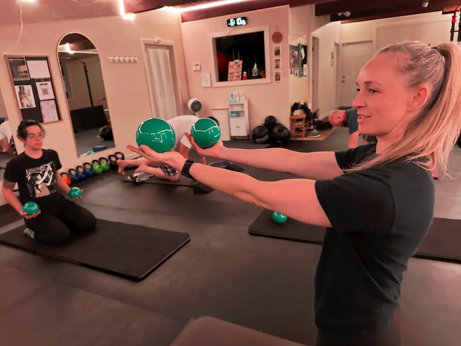 Allison holding green weights teaching a small group Pilates mat class in the studio.